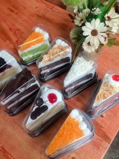 there are seven different desserts in plastic containers on the table next to a vase with flowers