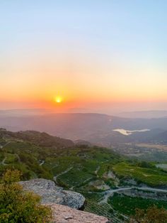 the sun is setting on top of a hill overlooking a valley and lake in the distance