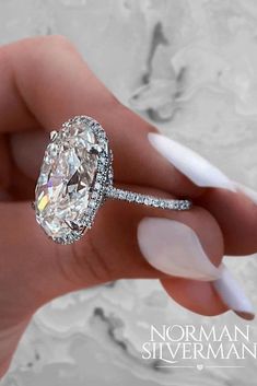 a woman's hand holding an oval shaped diamond ring with diamonds on the band