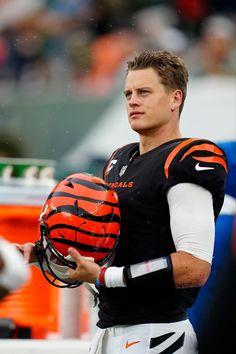 a man holding a football in his hand and wearing a helmet on the sidelines