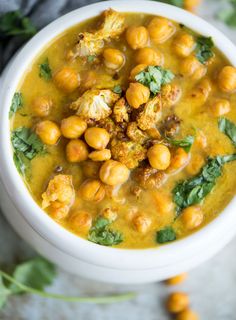 a white bowl filled with chickpeas and cauliflower soup on top of a table