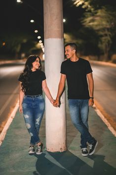 a man and woman standing next to each other on a street corner at night holding hands