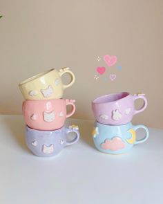 three cups sitting next to each other on top of a white table with pink, blue, and yellow designs