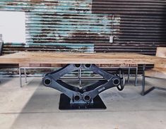 a wooden table sitting next to two chairs on top of a cement floor in front of a rusty wall