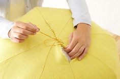 a woman is working on an umbrella with yellow fabric and thread as she sews it