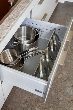 an open drawer with pots and pans on the bottom shelf in a kitchen area