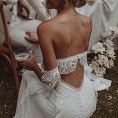 a woman in a white dress holding a wine glass and looking at the back of her dress