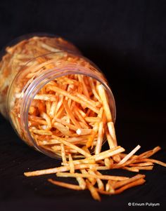 a jar filled with french fries sitting on top of a wooden table next to a black background