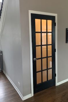 an empty room with a black door and wooden floors in front of a staircase leading up to the second floor