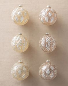 six glass ornaments are arranged in a row on a beige surface, with white and silver accents