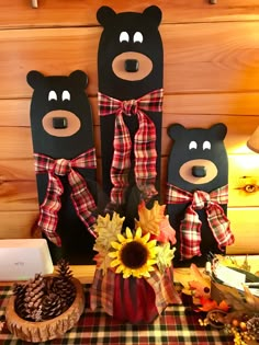 three black bears sitting on top of a table next to sunflowers and pine cones