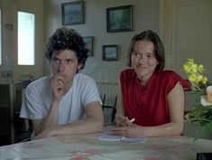 two people sitting at a table with flowers in the background