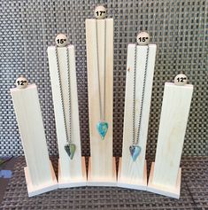 four necklaces are on display in front of a wooden stand with measurements for them