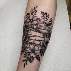 a black and white photo of a tattoo with books, flowers and leaves on it