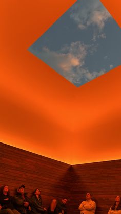 people are sitting in a room with orange walls and a blue sky above the ceiling