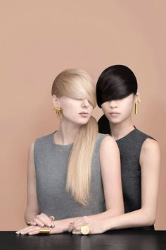 two women sitting next to each other at a table with their hair in ponytails