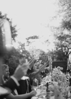 a group of people sitting at a long table with wine glasses in their hands,