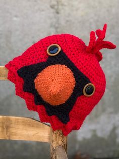 a crocheted red and black hat sitting on top of a wooden chair next to a cement wall