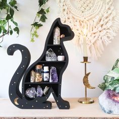 a black cat shaped shelf with crystals and rocks on it next to a candle holder