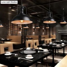 an empty restaurant with black tables and white plates on the table, lights hanging from the ceiling