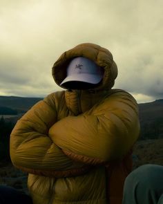 a person in a yellow jacket and hat with their arms crossed looking at the sky