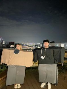 two people standing on a roof with their arms around each other and one person holding a cardboard box