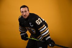 a man in black and gold jersey holding a hockey stick with both hands on his hip