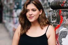 a woman standing next to a wall with graffiti on it's walls and looking at the camera