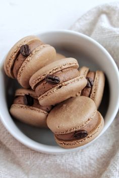 a white bowl filled with chocolate macaroons on top of a cloth covered table