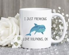 a white coffee mug with a dolphin on it next to flowers and a flower pot