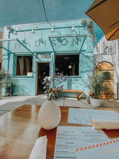 a table with papers and flowers on it in front of a blue building that has an open door