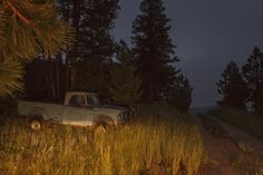 an old pick up truck is parked in the middle of a grassy field at night