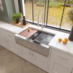 a stainless steel kitchen sink in front of a window with potted plants on the counter