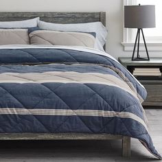 a bed with blue and white comforter in a bedroom next to a lamp on a table