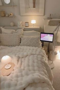 a bed with white blankets and pillows in a bedroom next to a laptop on a table