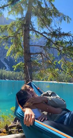 a man laying in a hammock next to a lake