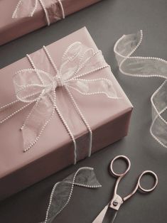 a pair of scissors sitting next to a pink present box with ribbon and bow on it