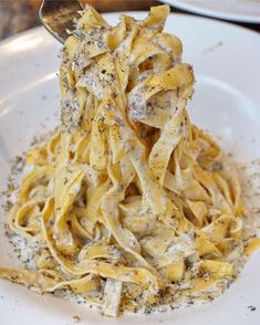 a white plate topped with pasta covered in grated cheese next to a silver spoon