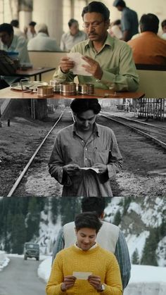 two people sitting at a table in front of a train track and another man standing next to them