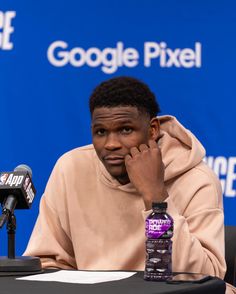 a man sitting in front of a microphone with his hand to his face while wearing a hoodie