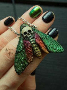 a woman's hand holding a green and red butterfly necklace with skull on it