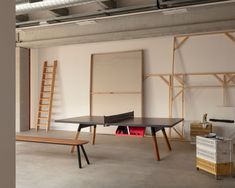 a ping pong table sitting in an empty room with ladders on the wall