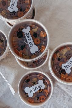 four plastic containers filled with dog treats on top of a white cloth covered tablecloth