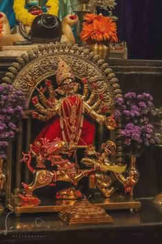 a statue of the hindu god sitting on a throne surrounded by flowers and other decorations