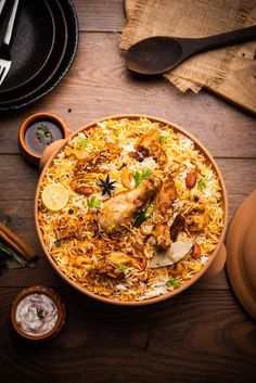 a large bowl filled with food on top of a wooden table next to utensils