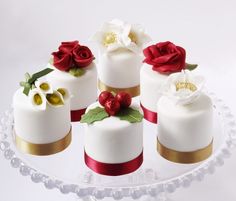 six small cakes decorated with red and white flowers on a clear cake platter,