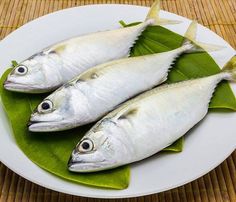 three fish are on a plate with green leaves