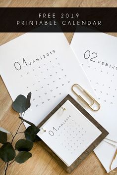 two calendars and a clipboard on top of a wooden table next to a plant