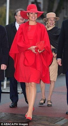 the woman is wearing a red hat and dress while walking down the street with other people