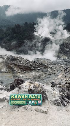 a sign that is sitting on the ground near some rocks and steam coming out of it